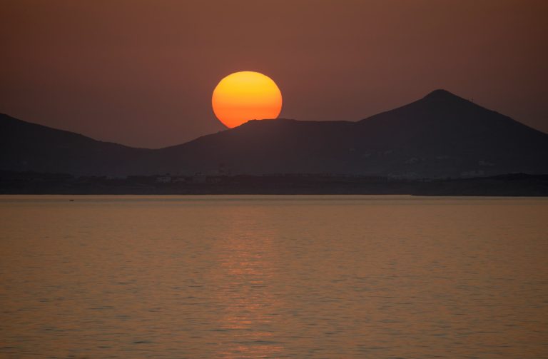 A beautiful sunset in Naxos. The sun sets behind the mountains and the calm sea.