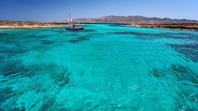 A magical green-blue sea with a small boat and people swimming in Antiparos-Despotiko.