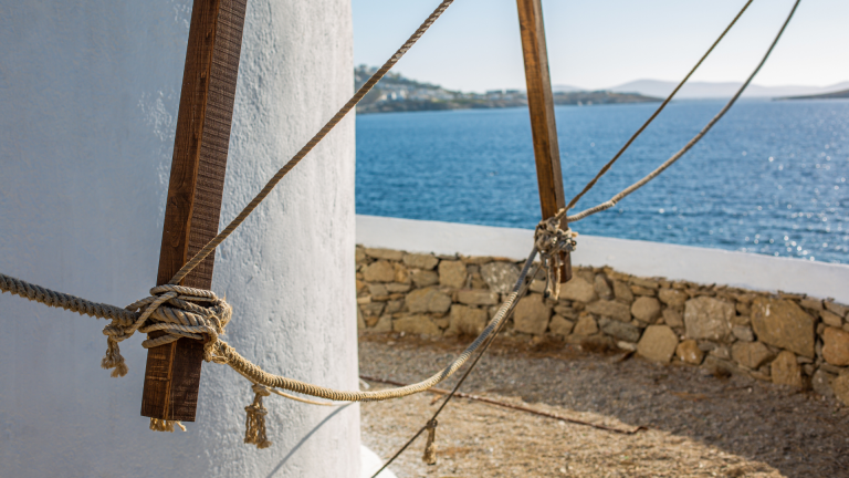 Taut ropes and a wooden support beam on a traditional Cycladic windmill overlooking the blue Aegean Sea near Delos and Mykonos.